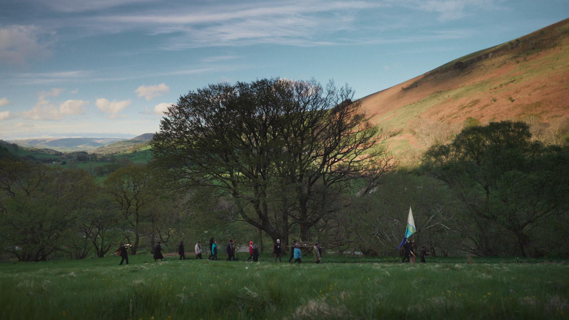 Groupe de personnes marchant dans une prairie au pied des collines sous un grand arbre