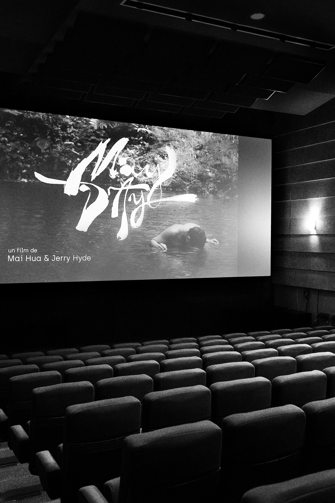 Salle de cinéma vide avec l’écran affichant le titre du film May Day en noir et blanc